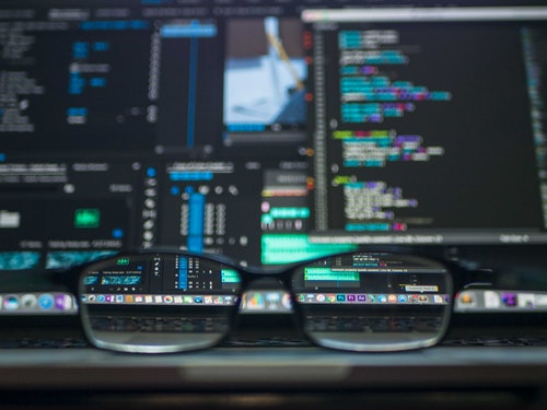 Glasses on desk in front of computer with code on the screen
